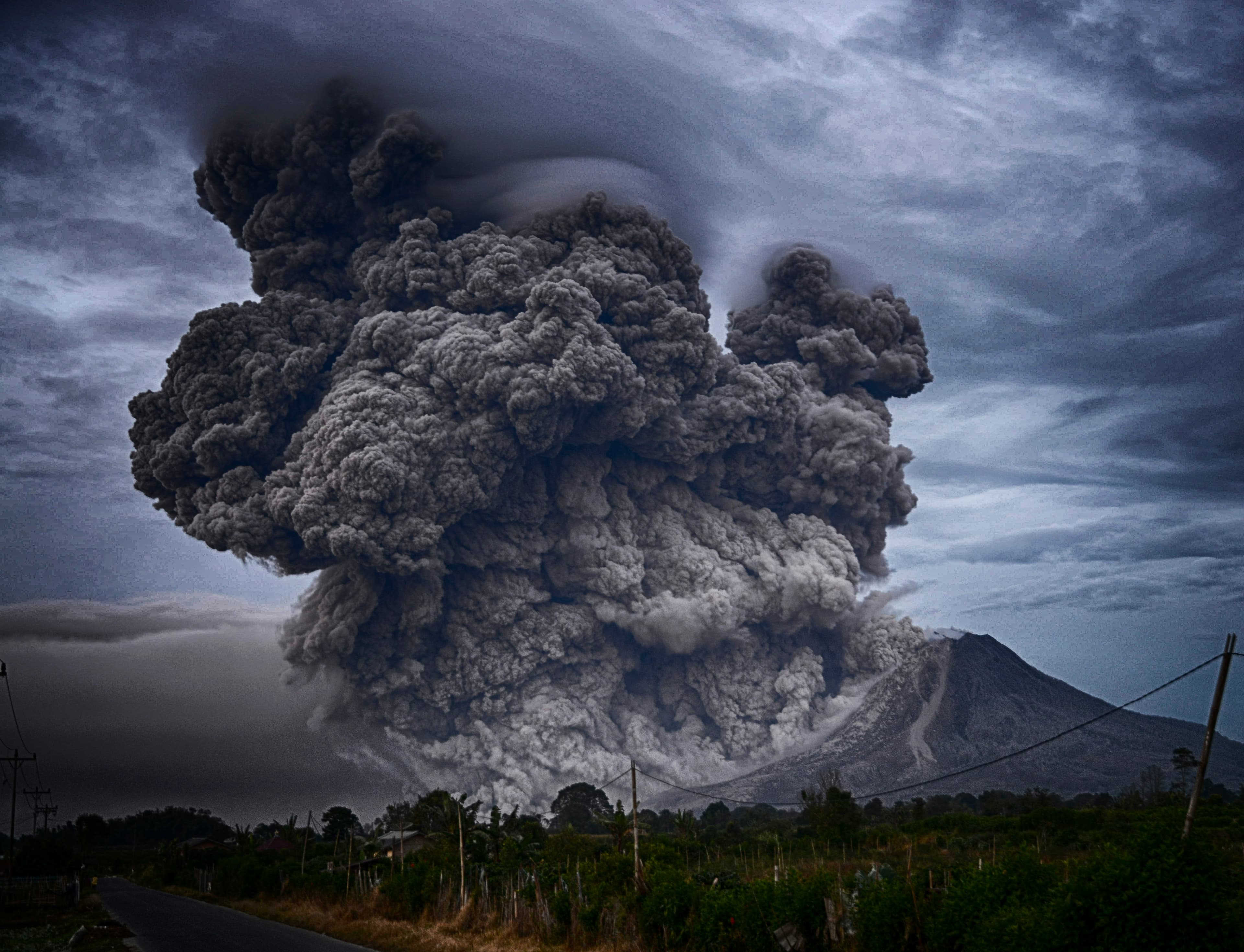 Volcanic ash cloud rising over a road and mountain landscape