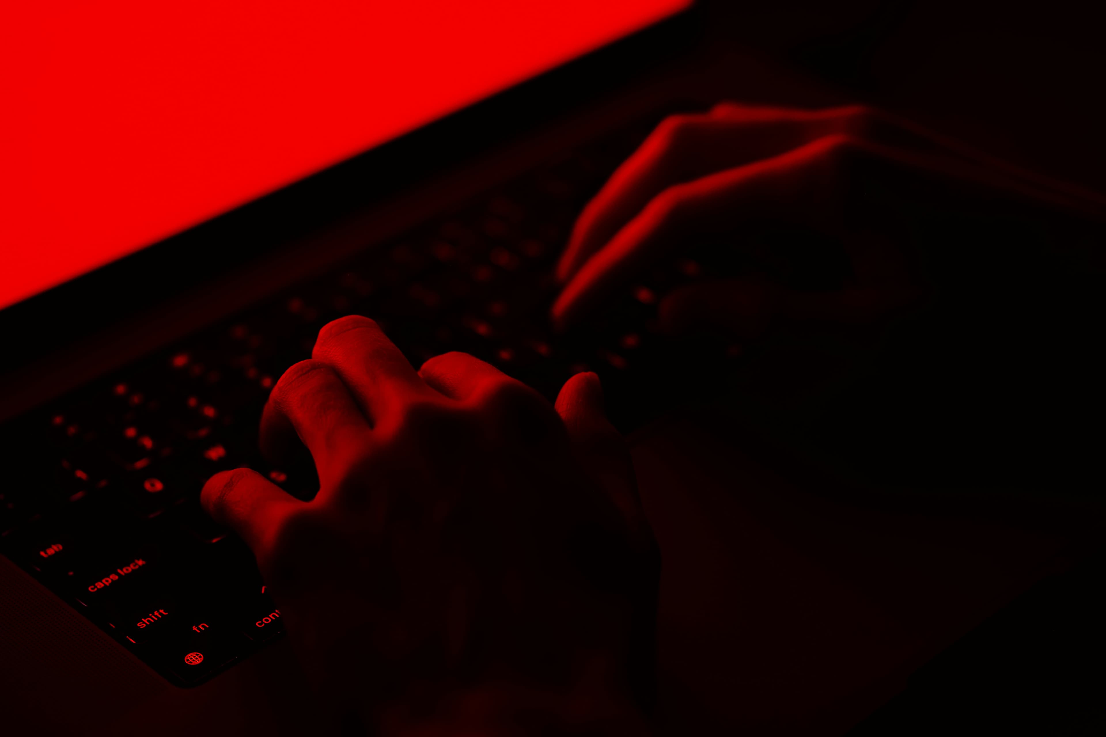 يدان تكتبان على لوحة مفاتيح حاسوب محمول تحت ضوء أحمر، بما يوحي بمراقبة التهديدات الرقمية
